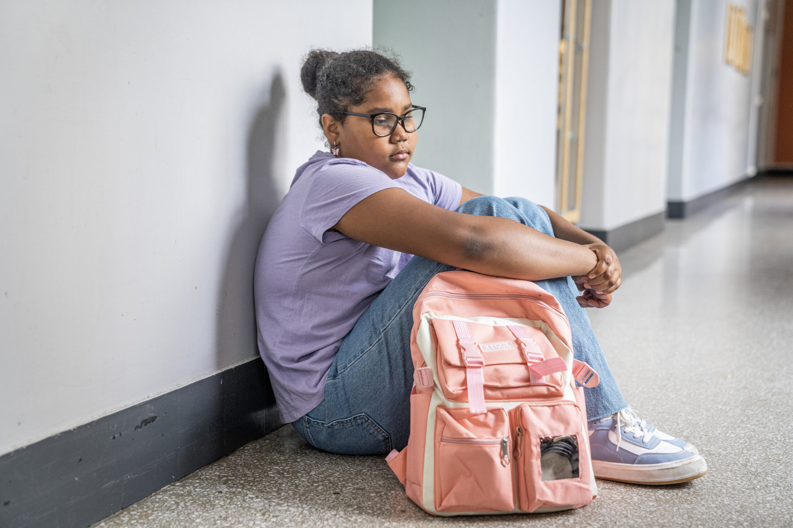 Illustrasjonsfoto av jente sitter alene i gangen på skolen.