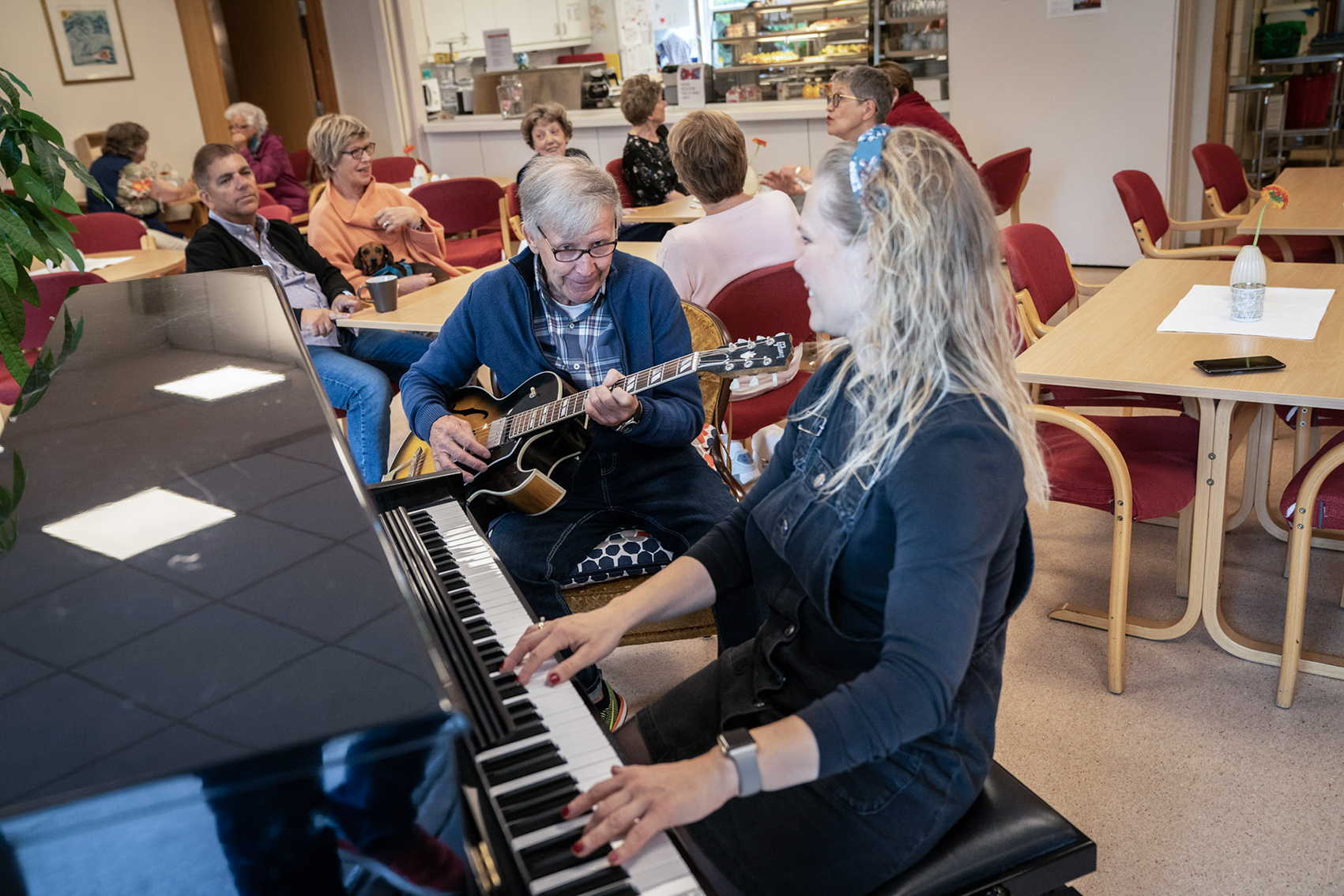 Eldre mann spiller gitar og ansatt spiller piano for fellesskapet