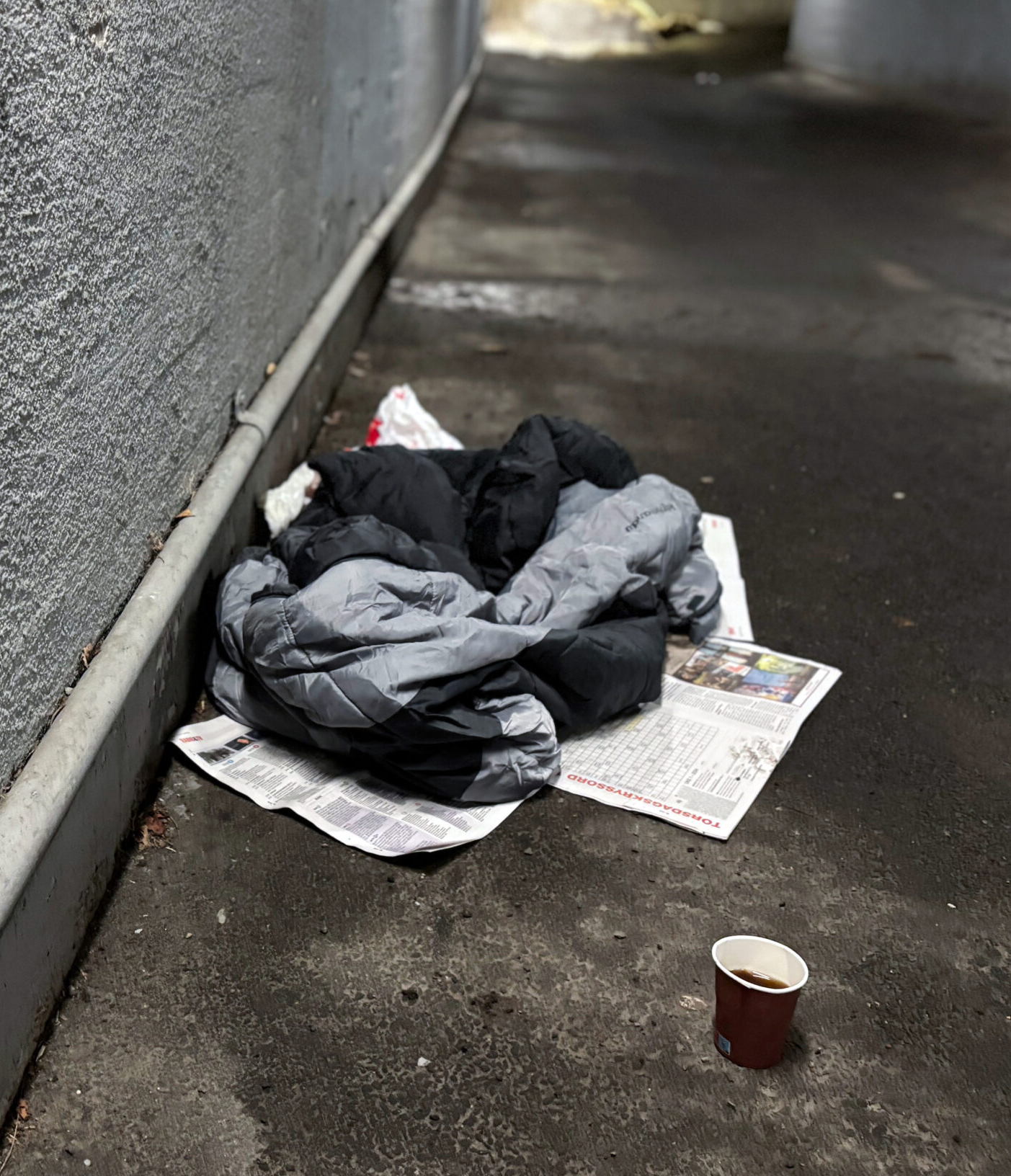 Bostedsløse - sovepose på bakken under en tunnel og et pappkrus med kaffe