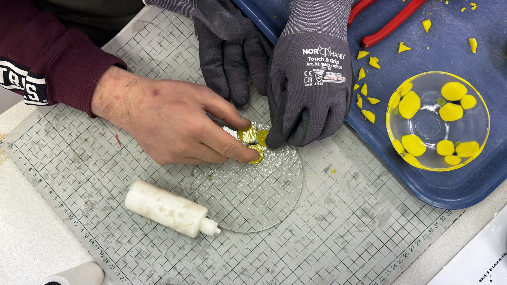 Hendene til Bj&oslash;rn som lager glassprodukt. En glass-sk&aring;l med gule stemorsblomster ligger ogs&aring; p&aring; arbeidsbenken.