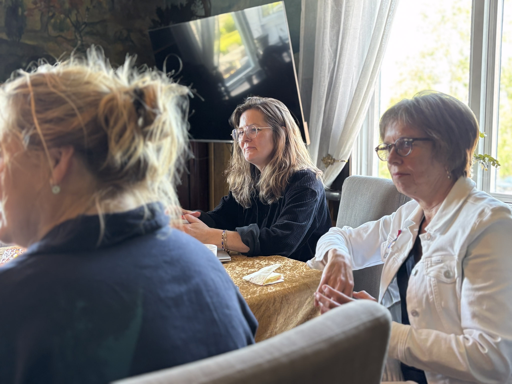 To kvinner (Elisabeth og Heidi) sitter ved et bord og lytter til noe som blir sagt