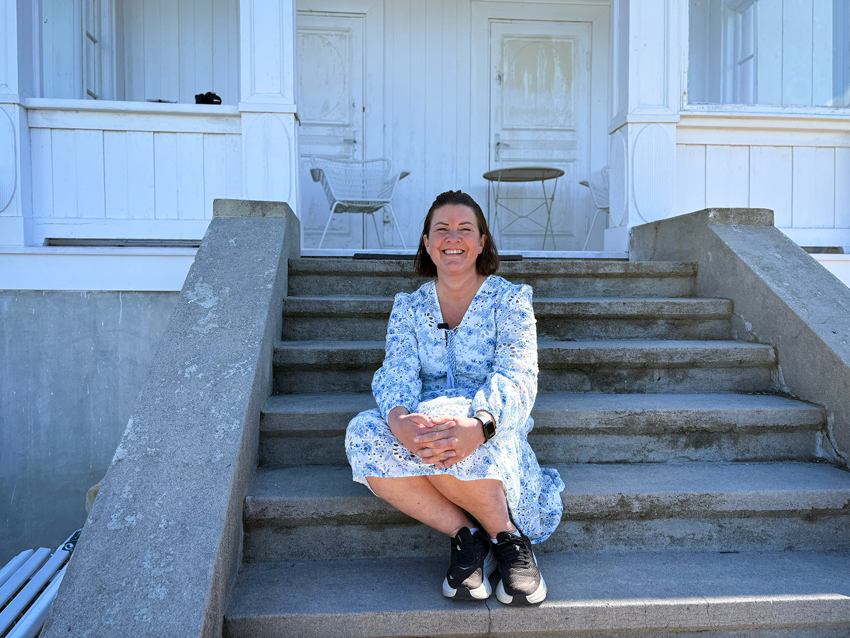 En smilende kvinne sitter p&aring; en trapp
